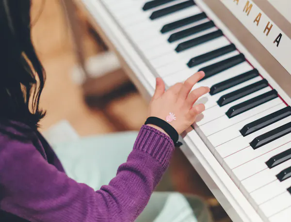 A young girl sits at a piano and plays a key.