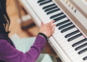 A young girl sits at a piano and plays a key.