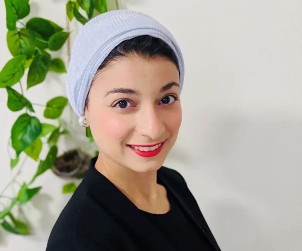 Dietitian Lina Breik wears a headscarf over her dark hair and smiles at the camera. A plant hangs in the background.