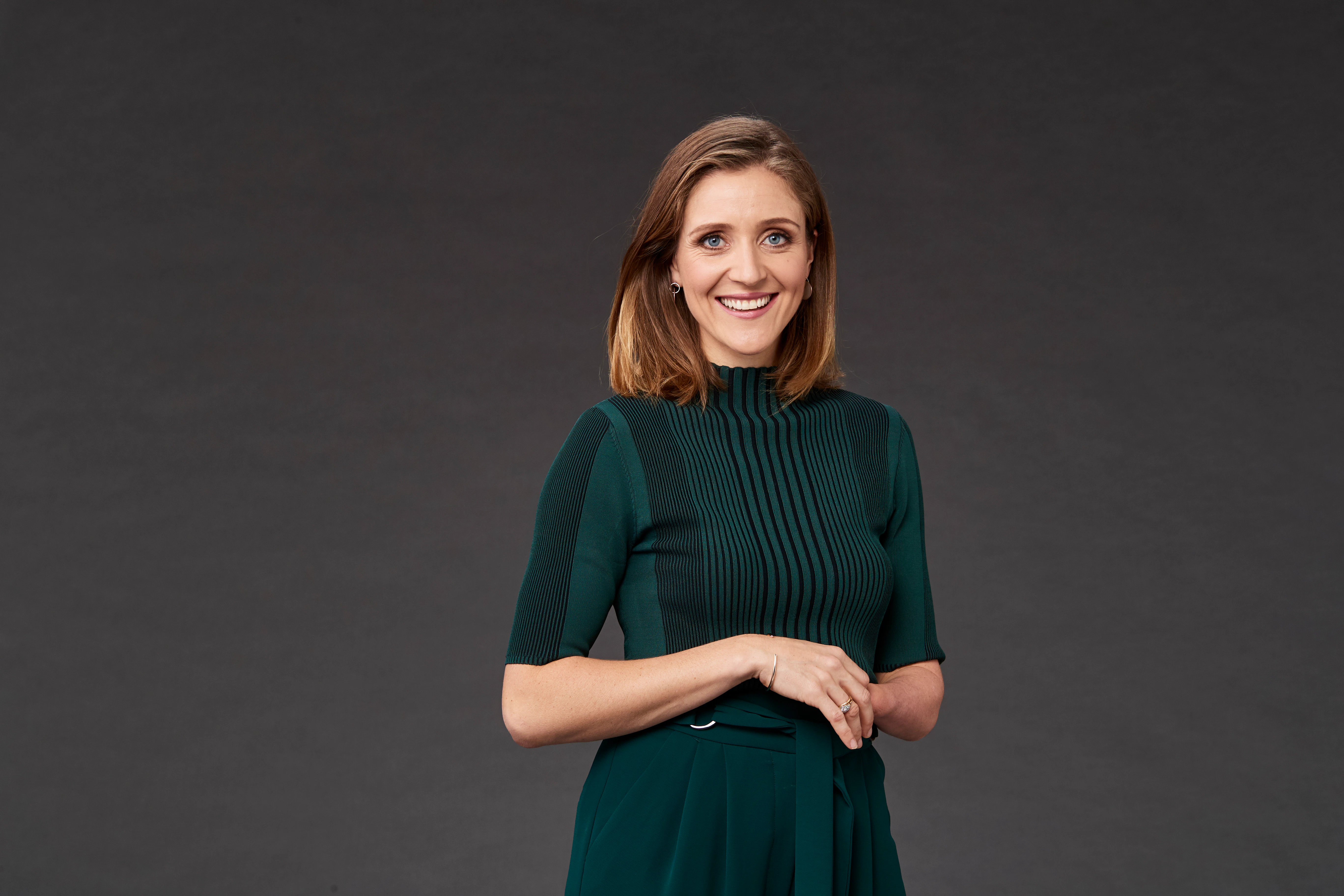 Paralympian Annabelle Williams is standing smiling at the camera with her arms folded across her stomach. She has shoulder length brown hair and is wearing a bottle green top and pants.