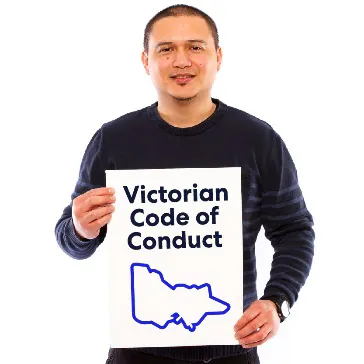 A man holding a poster labelled 'Victorian Code of Conduct' with a map of Victoria.