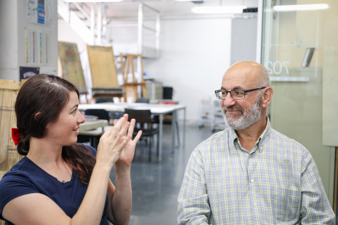 Jess is signing to Joe using AUSLAN. They're sitting in Joe's art studio. 