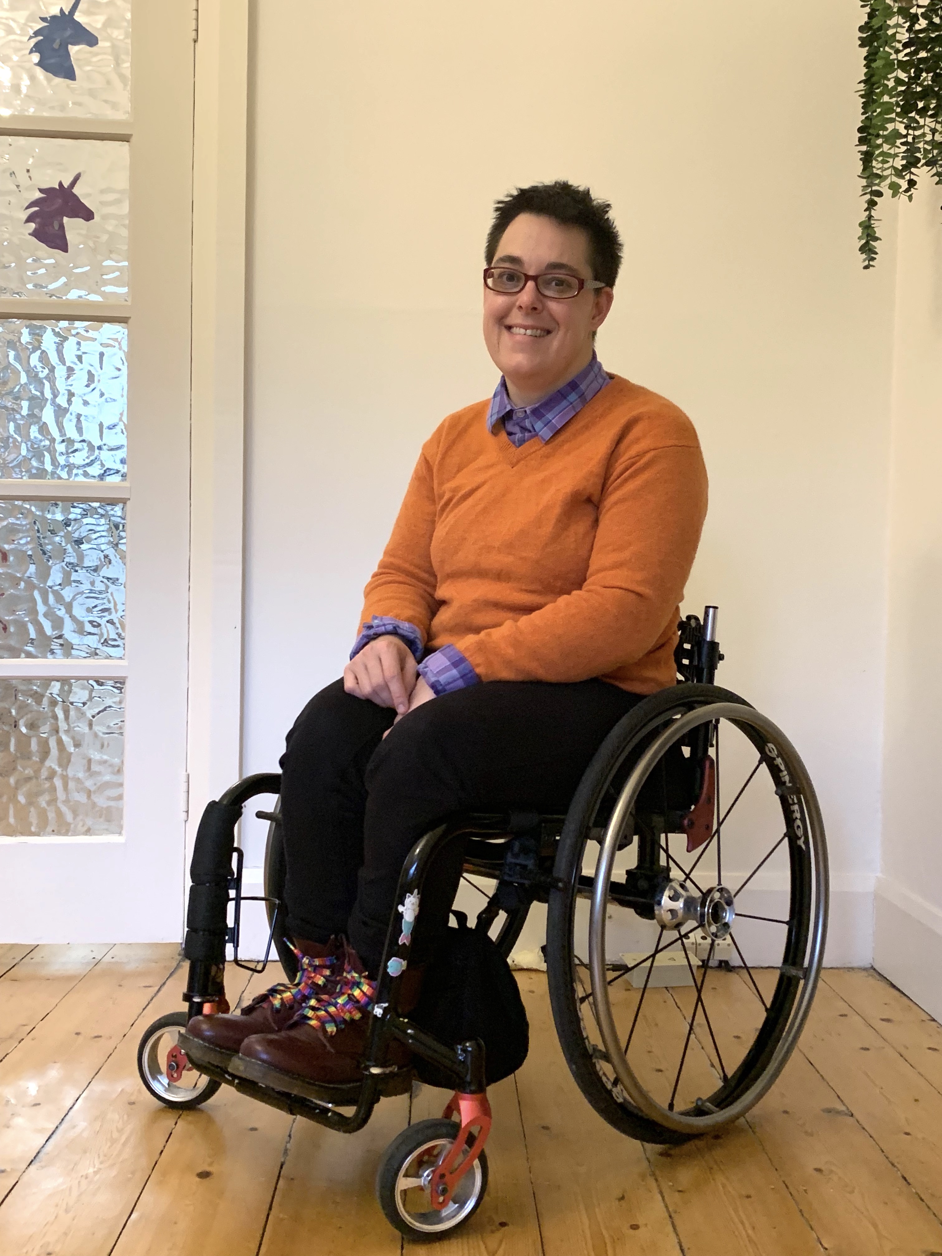 Jax is wearing a bright orange jumper with a collared shirt poking through. Jax is a wheelchair user. 