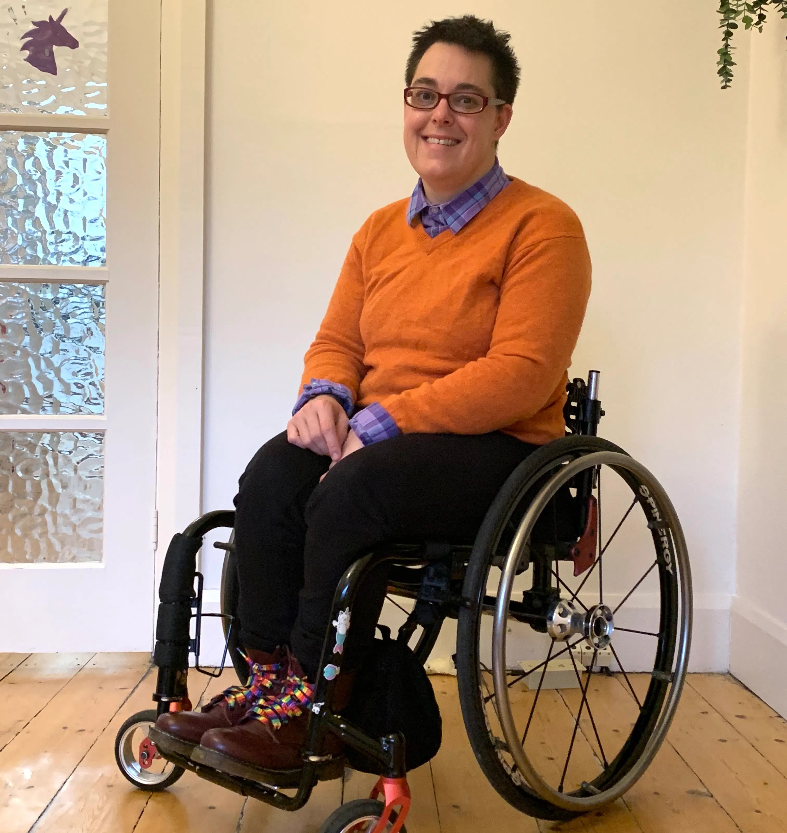 Jax is wearing a bright orange jumper with a collared shirt poking through. Jax is a wheelchair user.