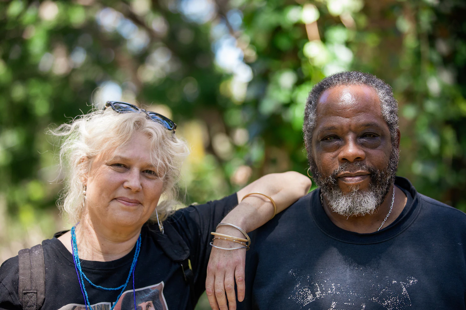 Caroline and Pat are both standing in front of a tree. They are smiling and Caroline ha her arm on Pat's shoulder.