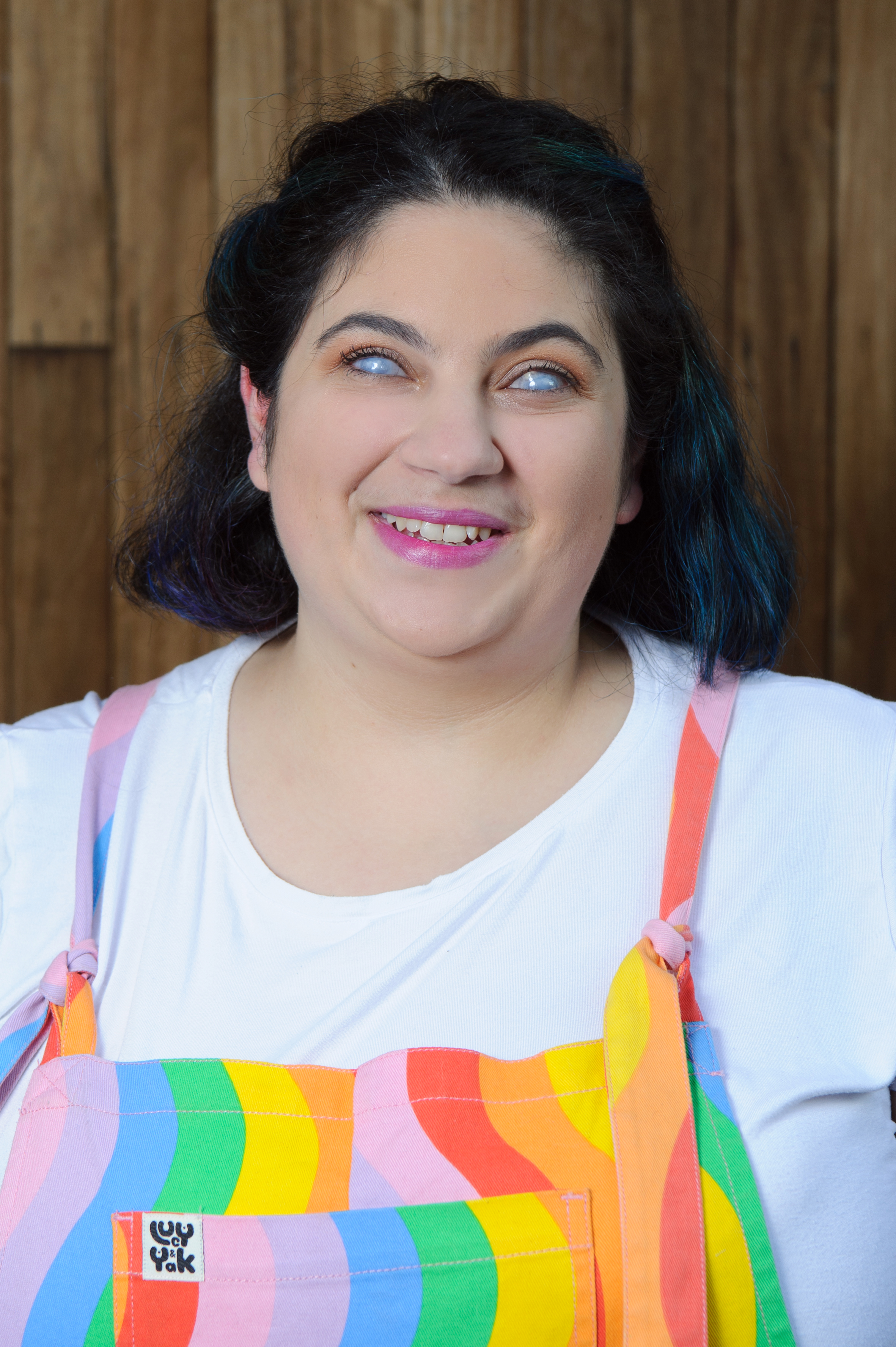 Freelance artist Olivia Muscat has short, dark brown hair. She wears vibrant makeup and rainbow-coloured overalls with white t-shirt.