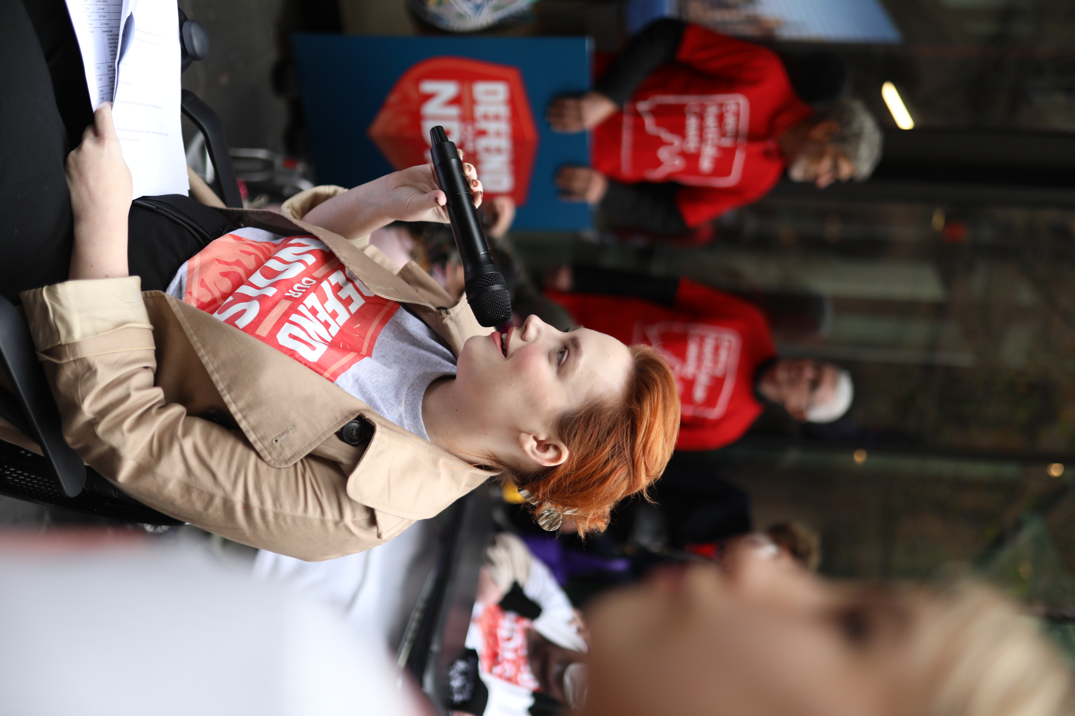 Elly sits and talks into a microphone at the Defence our NDIS rally 