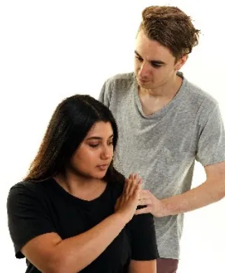 A woman is sitting down and holding her hand up to signal stop to a man who is behind her. He is resting his hand on her shoulder.