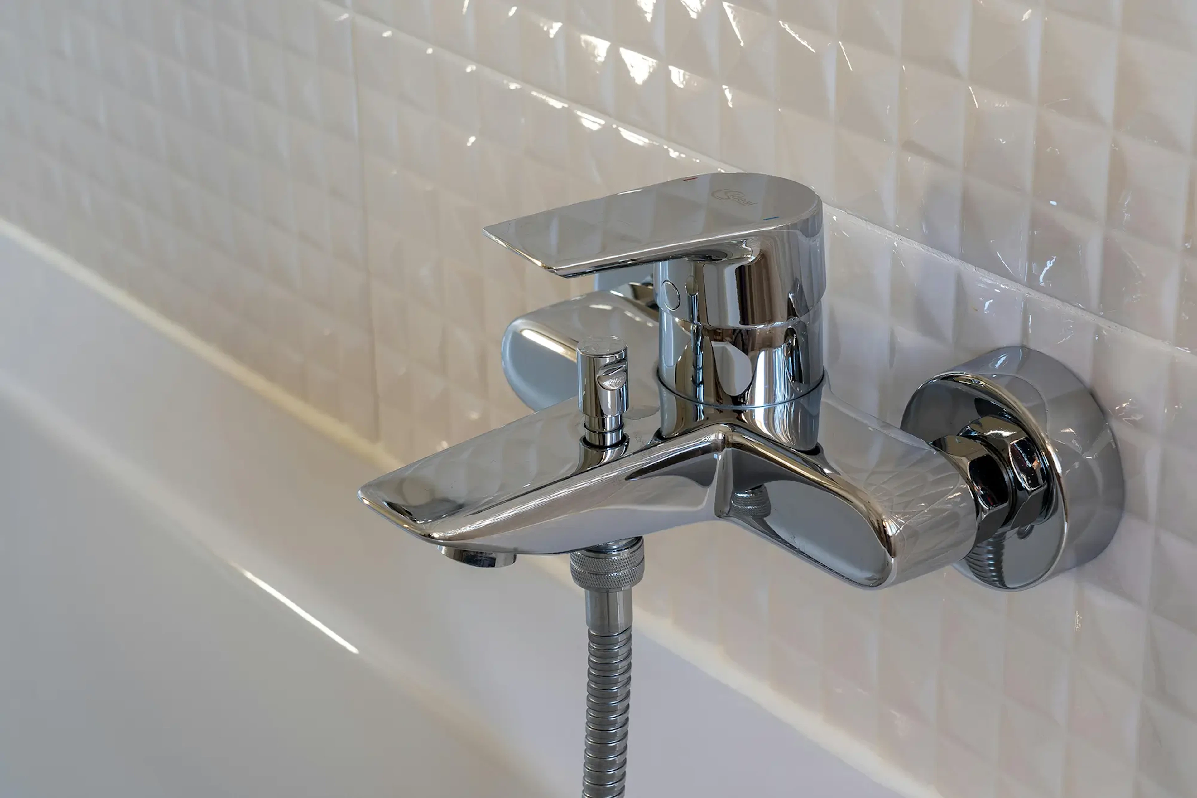 Shiny chrome-colored faucet against white tile