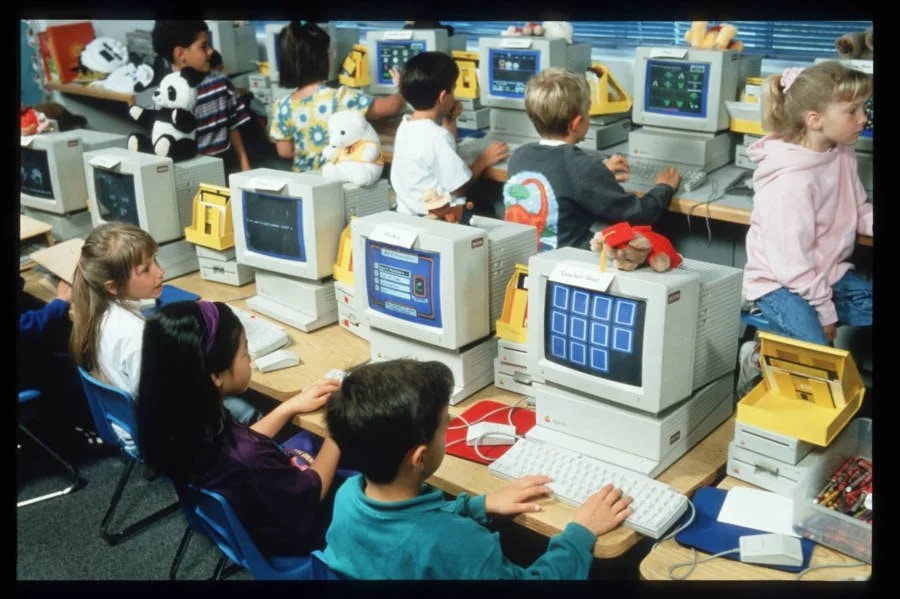 Vintage photo of elementary school children working in a computer lab full of early-model Apple computers.