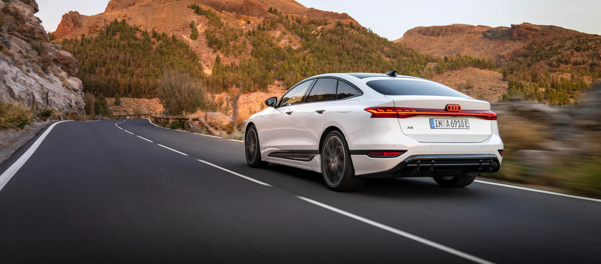 Audi A6 e-tron in Weiß bei Fahrt auf Bergstraße vor markanter Felslandschaft