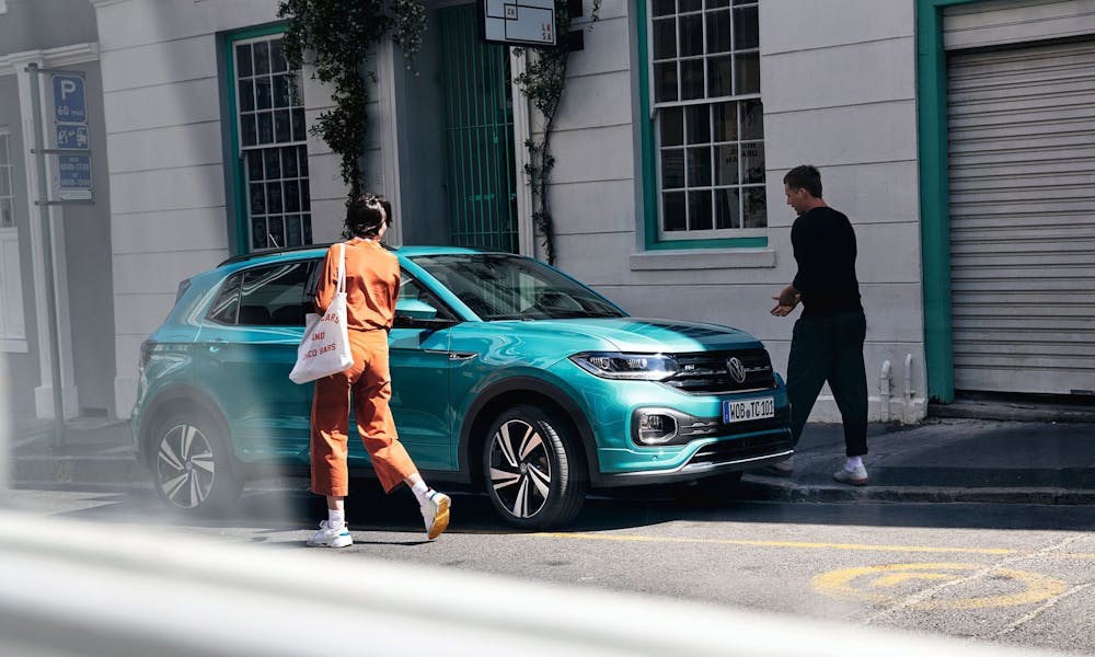 Zwei Personen neben vor Gebäude geparktem VW T-Cross