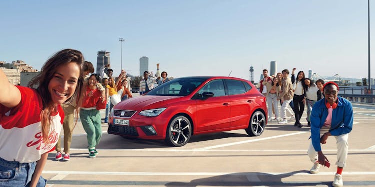 Personengruppe posiert rund um roten SEAT Ibiza