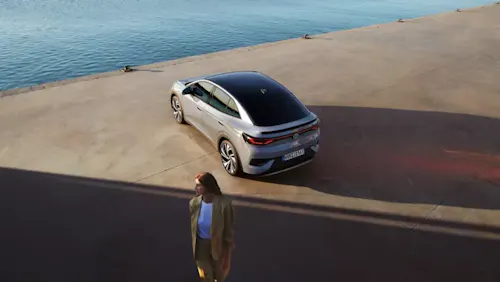 Frau läuft neben einem am Wasser geparkten VW ID.5