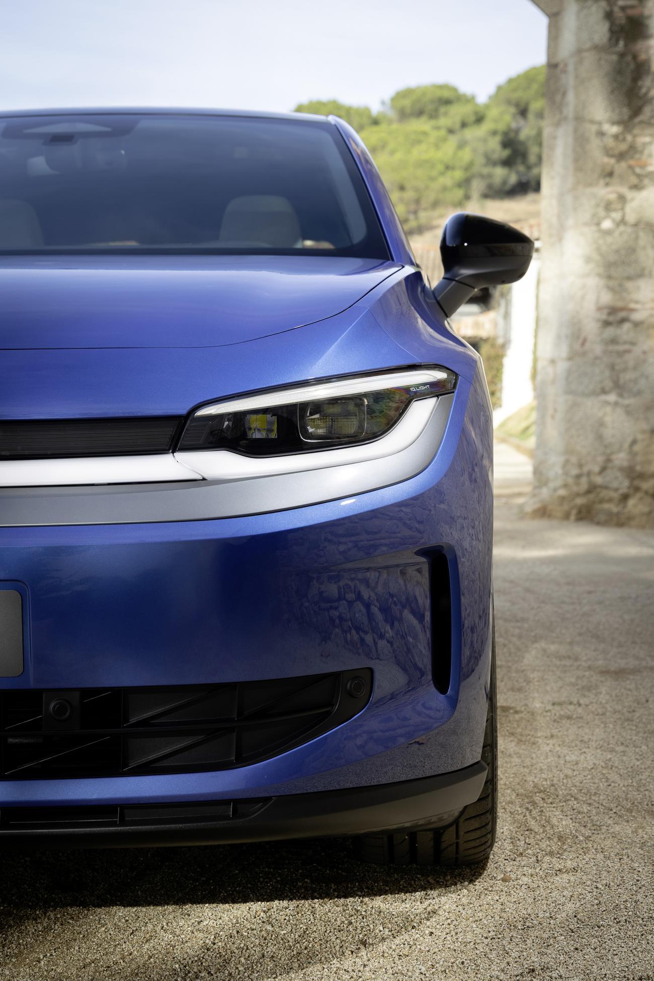 VW Elektroauto ID. Polo in Blau, Nahaufnahme der Frontpartie mit schlankem LED-Scheinwerfer und sportlicher Stoßstange vor mediterranem Steingebäude