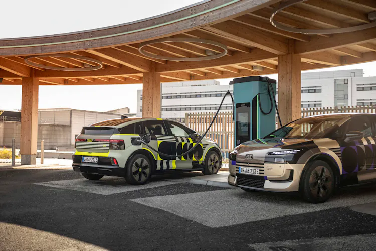 Zwei Audi A2 e-tron mit Designfolierung beim Laden an einer Schnellladesäule unter einem Holzdach