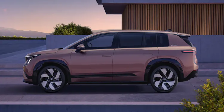 Škoda Peaq in Rosewood Beige Metallic, Seitenansicht vor moderner Holzfassade in der Abenddämmerung