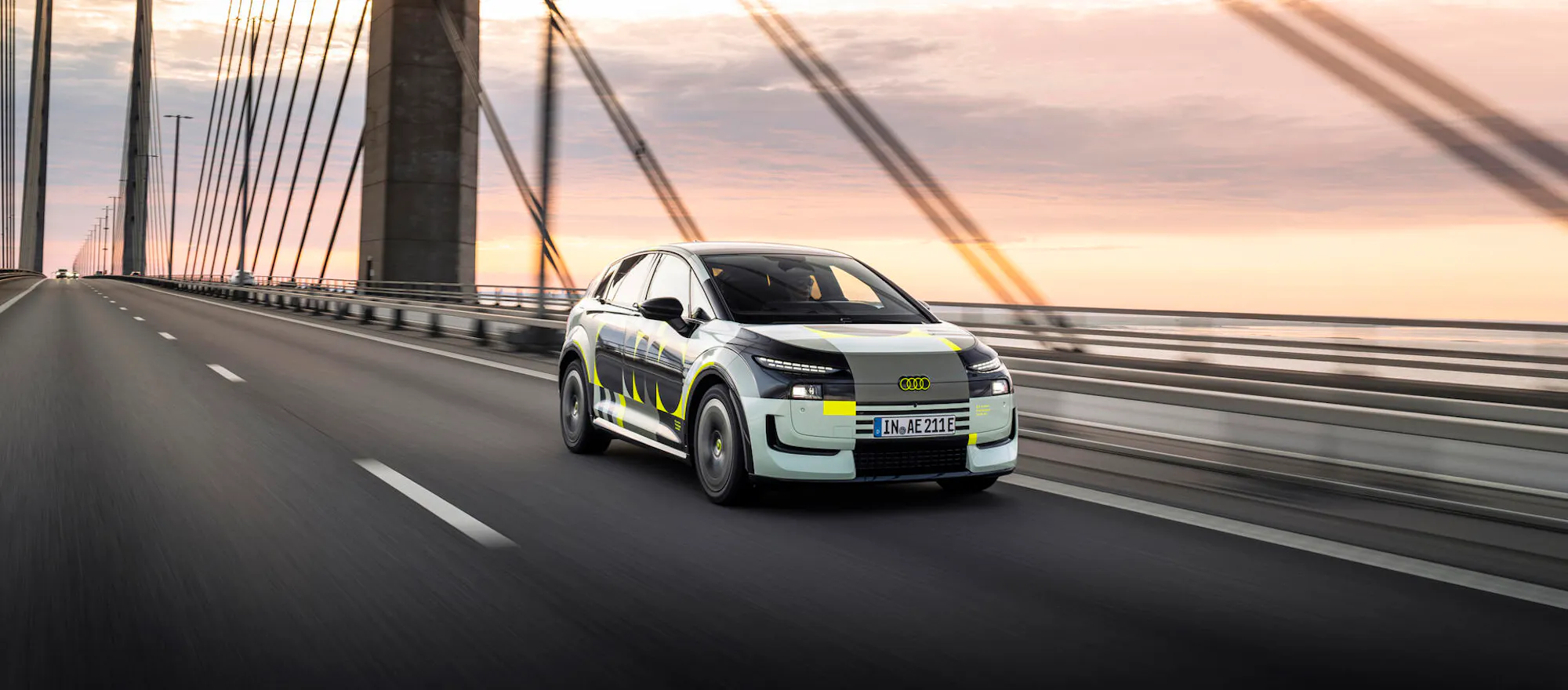 Audi A2 e-tron Prototyp mit Tarnfolierung bei Testfahrt auf Brücke bei Sonnenuntergang, Dreiviertelfrontansicht
