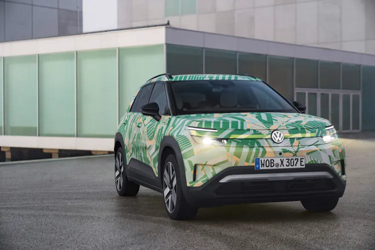 VW ID Cross Prototyp mit Tarnfolierung, Dreiviertelfrontansicht vor moderner Glasfassade