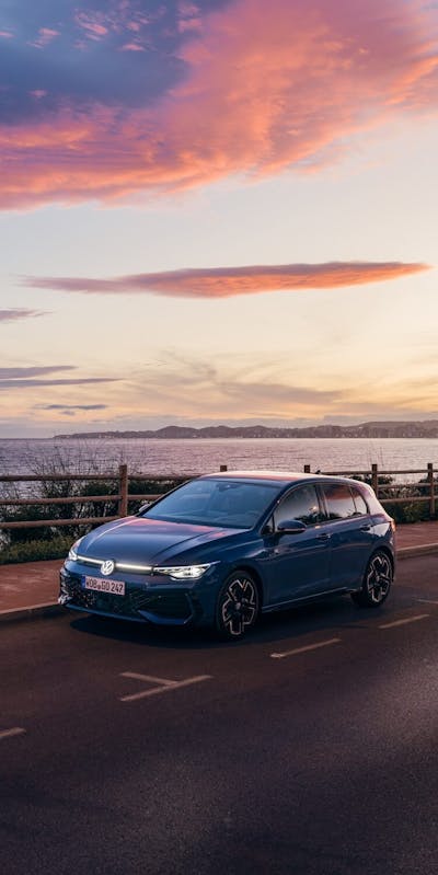 VW Golf auf der Straße mit Meer im Hintergrund bei Sonnenuntergang