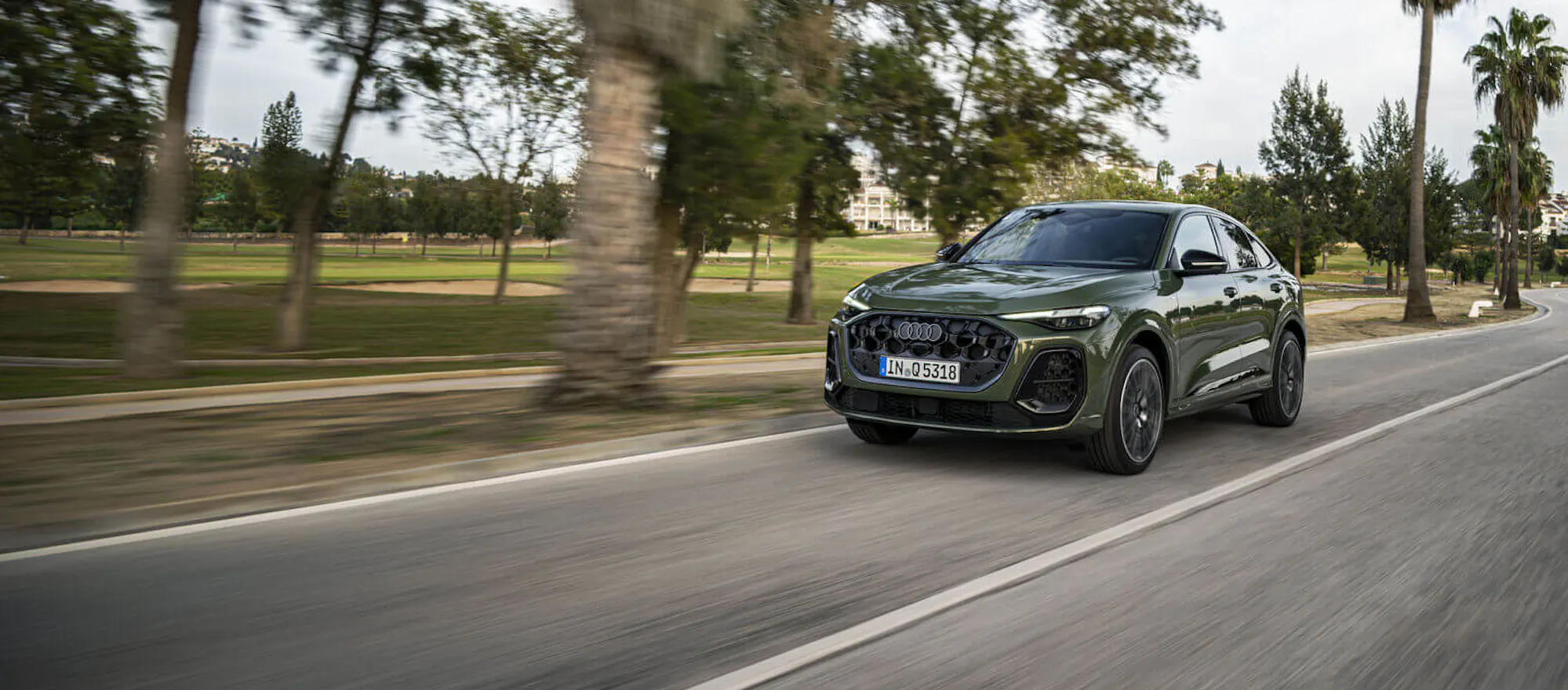 Audi Q5 in distriktgrün metallic, der auf einer Straße fährt