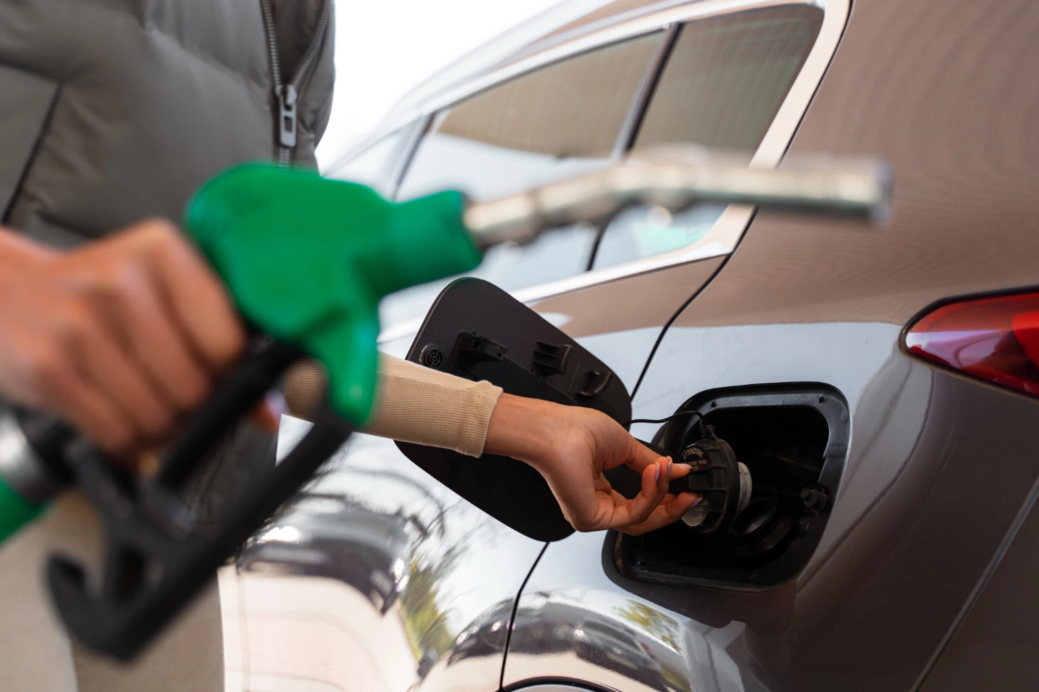 Frau betankt ein graues Auto an der Tankstelle – Tipps zum Sprit sparen