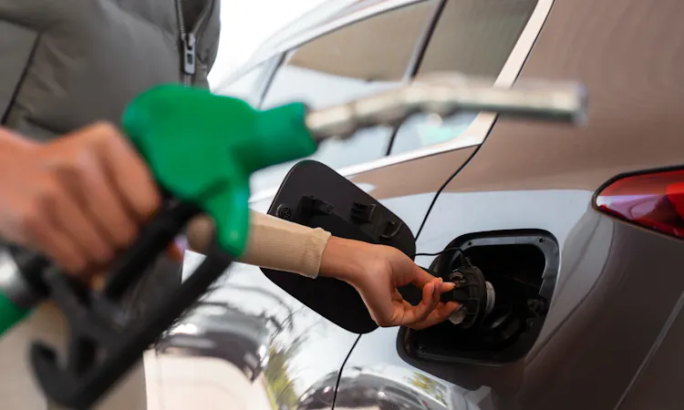 Frau betankt ein graues Auto an der Tankstelle – Tipps zum Sprit sparen