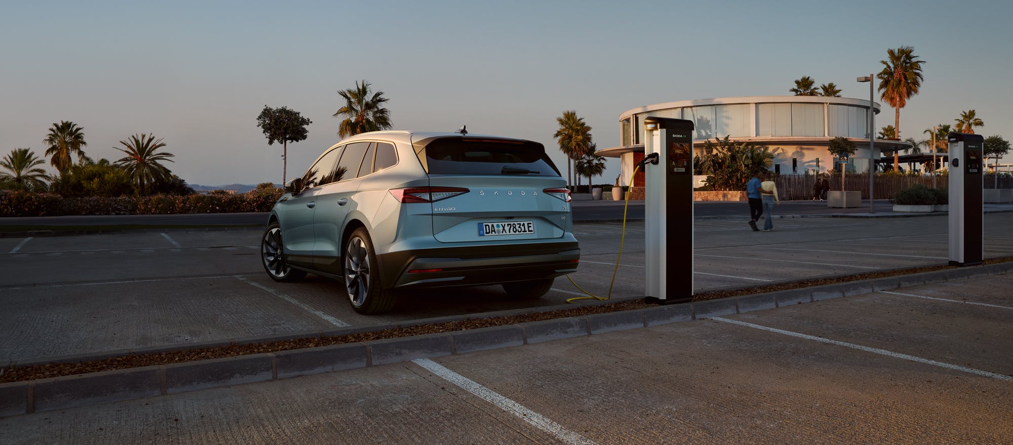 ŠKODA Enyaq an der Ladestation auf einem Parkplatz mit Palmen im Hintergrund