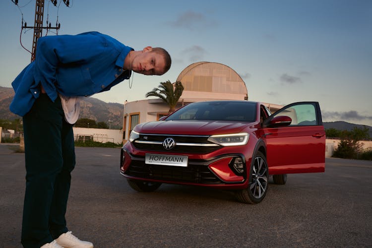 Mann steht nach vorne gebeugt vor rotem VW Taigo