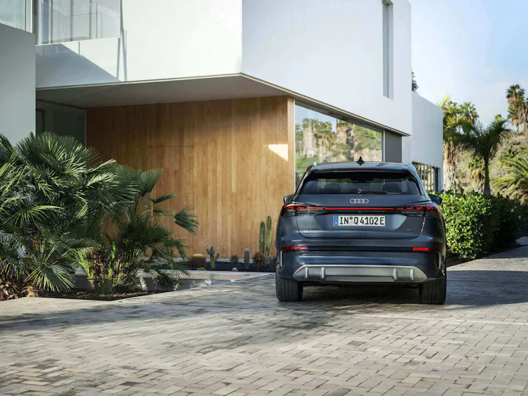 Audi Q4 e-tron – vollelektrisches SUV in Plasmablau in der Heckansicht vor moderner Villa