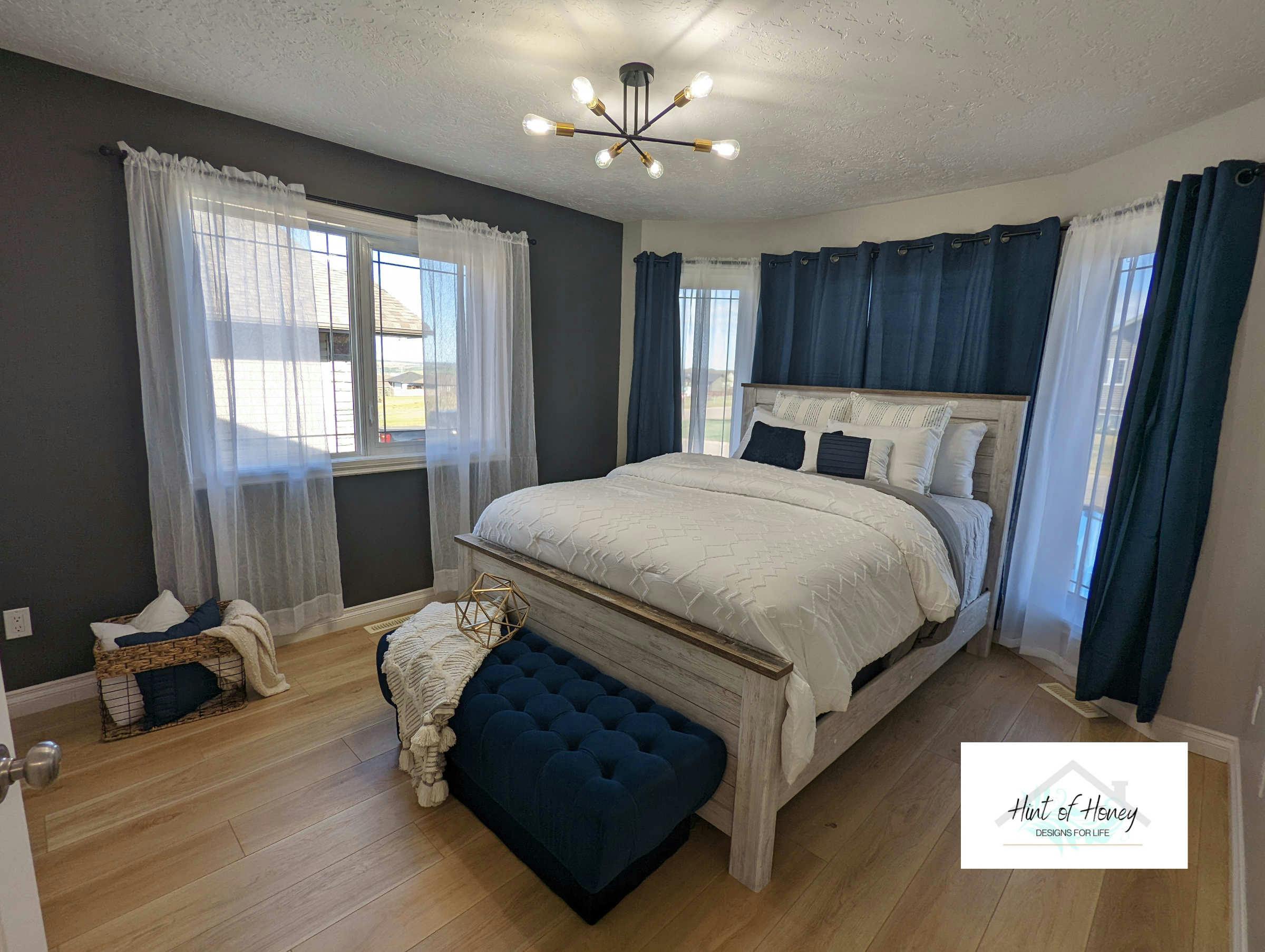 Master bedroom with large rustic wood bedframe and white and blue curtains