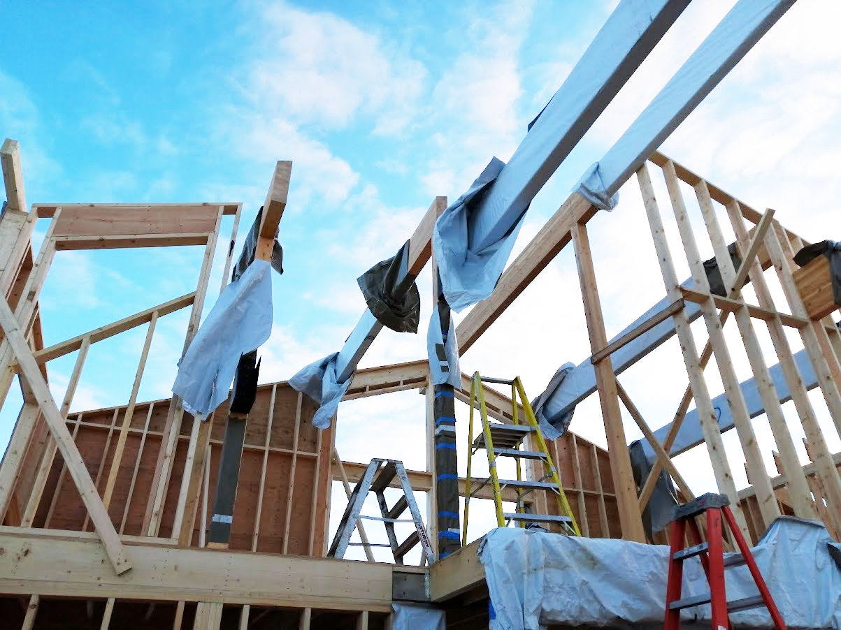 House under construction in framing stage. Beams open to blue sky