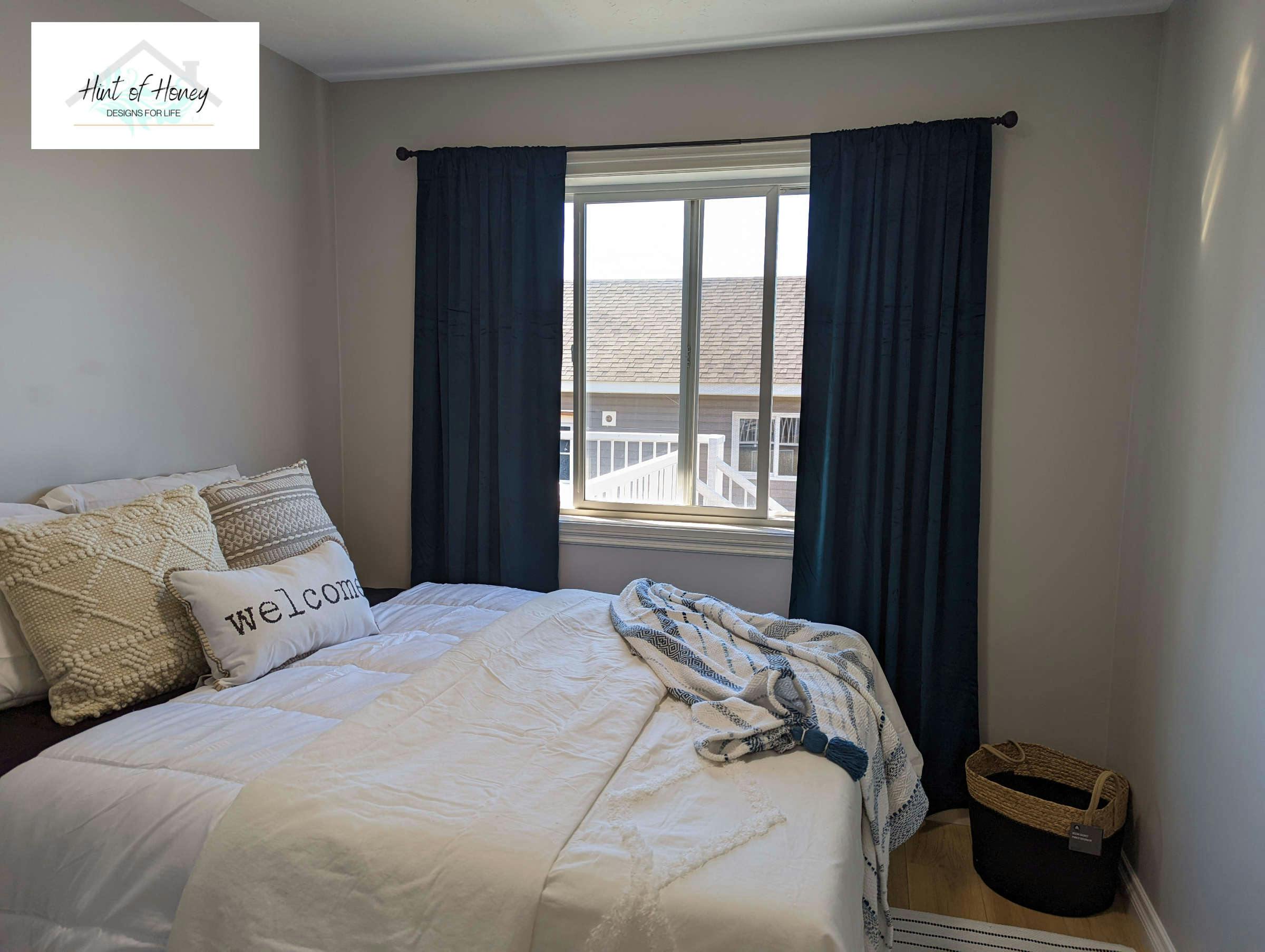 Bedroom with blue curtains and large plush bed with white sheets and throw pillows