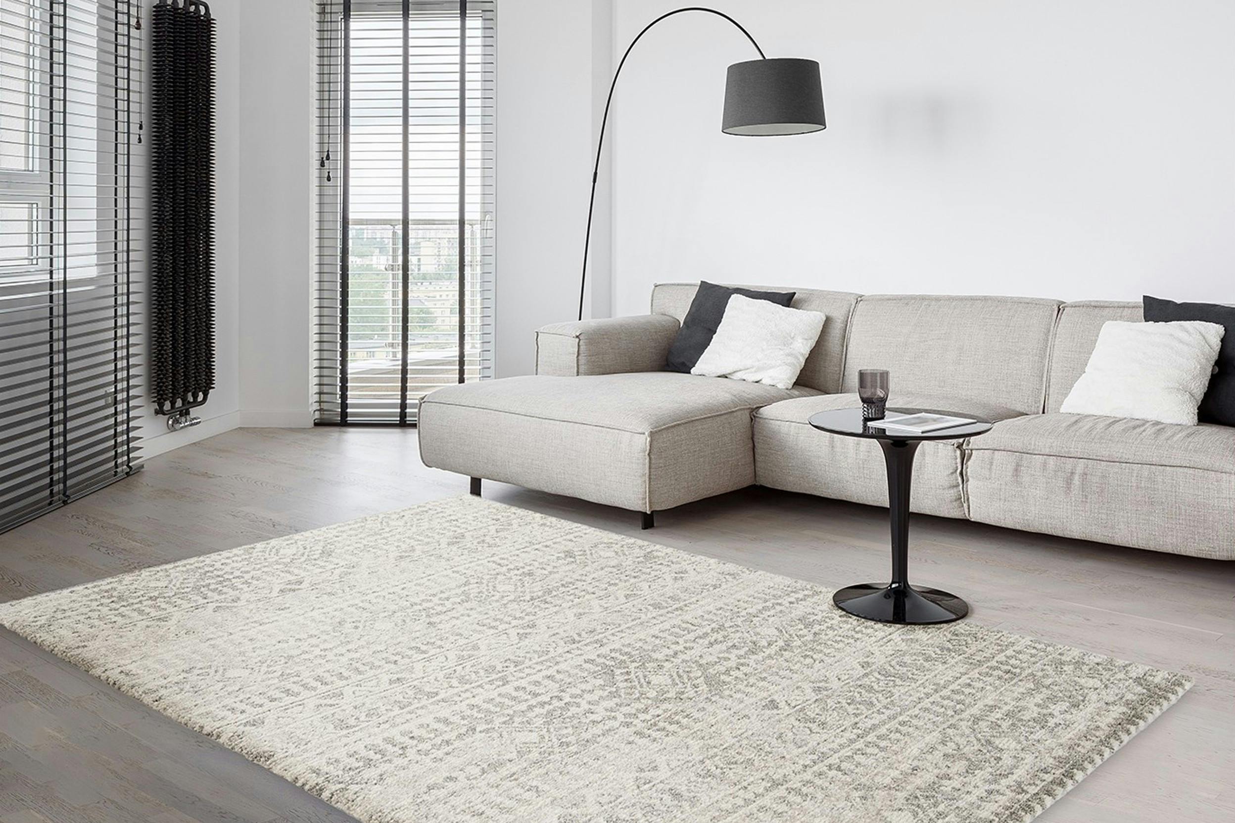 Grau gemusterter Teppich in minimalistischem Wohnzimmer mit hellgrauem Sofa und schwarzer Bogenlampe sowie Beistelltisch