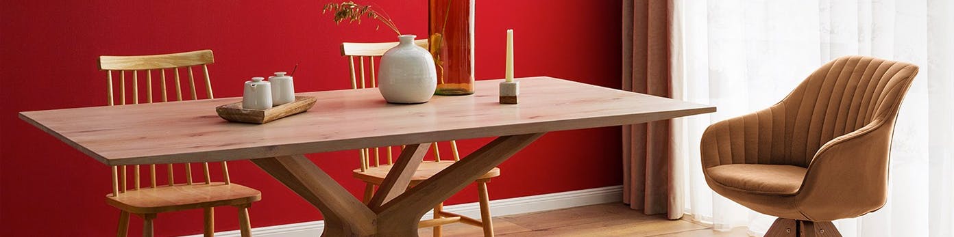 Holztisch mit darauf stehender Vase, Deko und Kerze und daran stehender gemütlicher Polsterstuhl und zwei Esszimmerstühle aus Holz