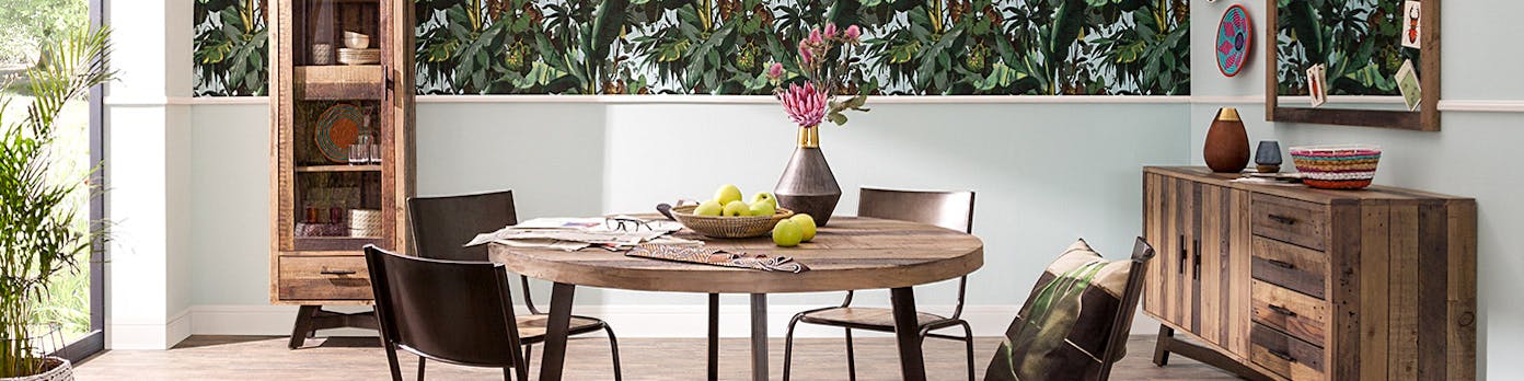 Esszimmer mit Holzmöbeln im Industrial-Stil vor Tapete mit Dschungel-Print