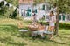 Klassische Holzklappmöbel inmitten eines sonnigen, grünen Gartens mit geschwungenen Lehnen, weißer Wimpelkette über dem Tisch und zwei Frauen, die den Tisch decken