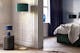 Chambre avec une lampe, un lampadaire et une suspension aux abat-jours en tissu vert, noir et bleu, lit capitonné de velours vert.