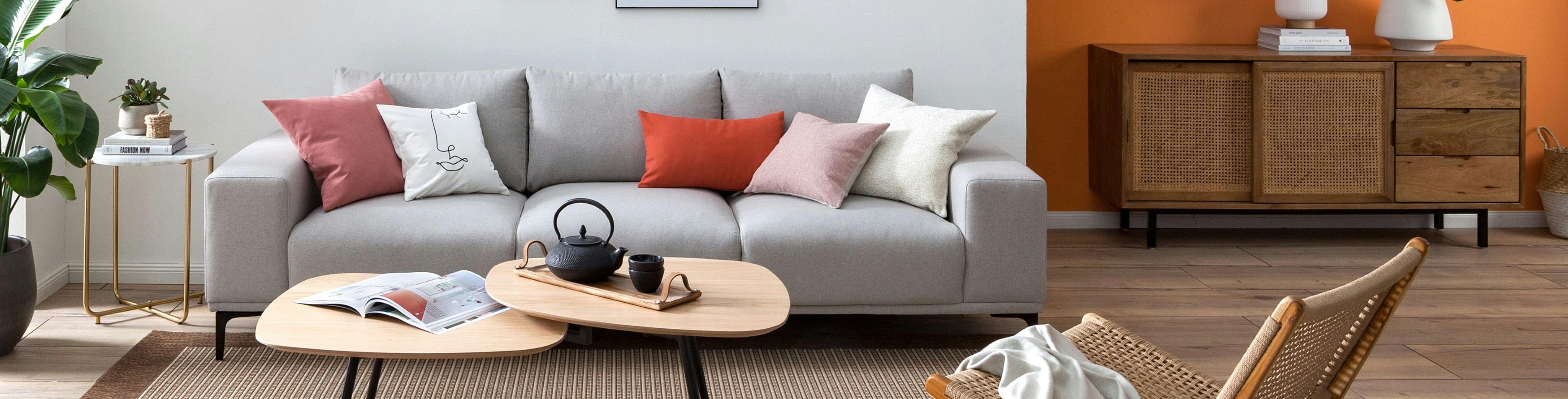 Offener Wohnbereich mit grauem Sofa, Satztischen, Loungesessel und Sideboard