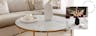 Woonkamer met beige interieur met als middelpunt een salontafel met wit marmeren tafelblad en gouden meubelpoten.