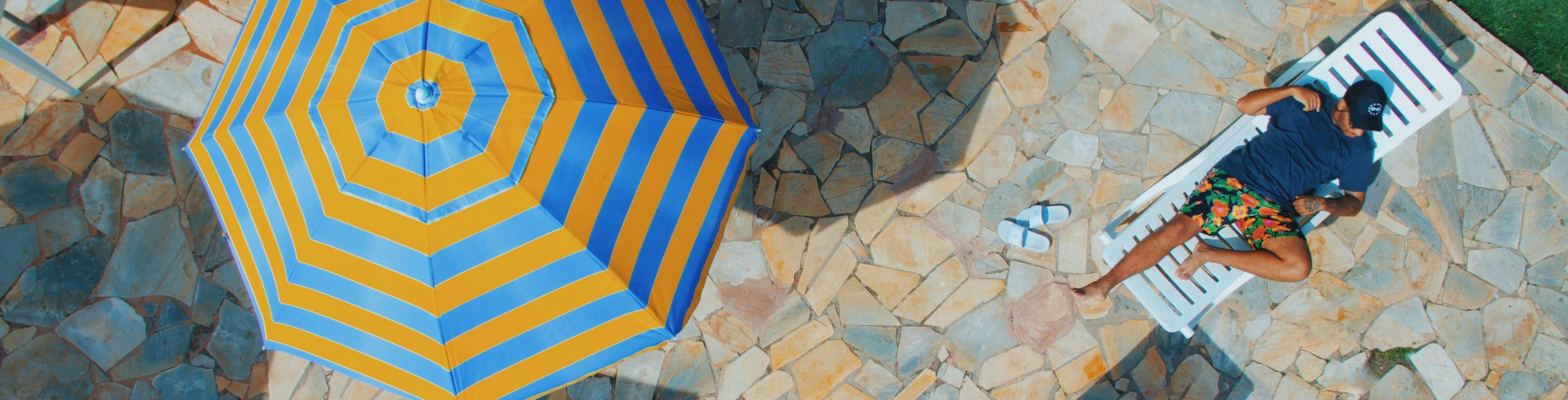 Gestreifter Sonnenschirm auf einer Steinterrasse zusammen mit einem Mann beim Sonnenbaden