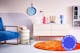Enfilade blanche Mørteens associée à des couleurs vives et des formes originales typiques du « dopamine decor » : un téléphone rétro rose, une lampe de table bleu clair, un vase BUTLERS rose, un tapis orange et un canapé en velours bleu home24 avec des accoudoirs dorés.