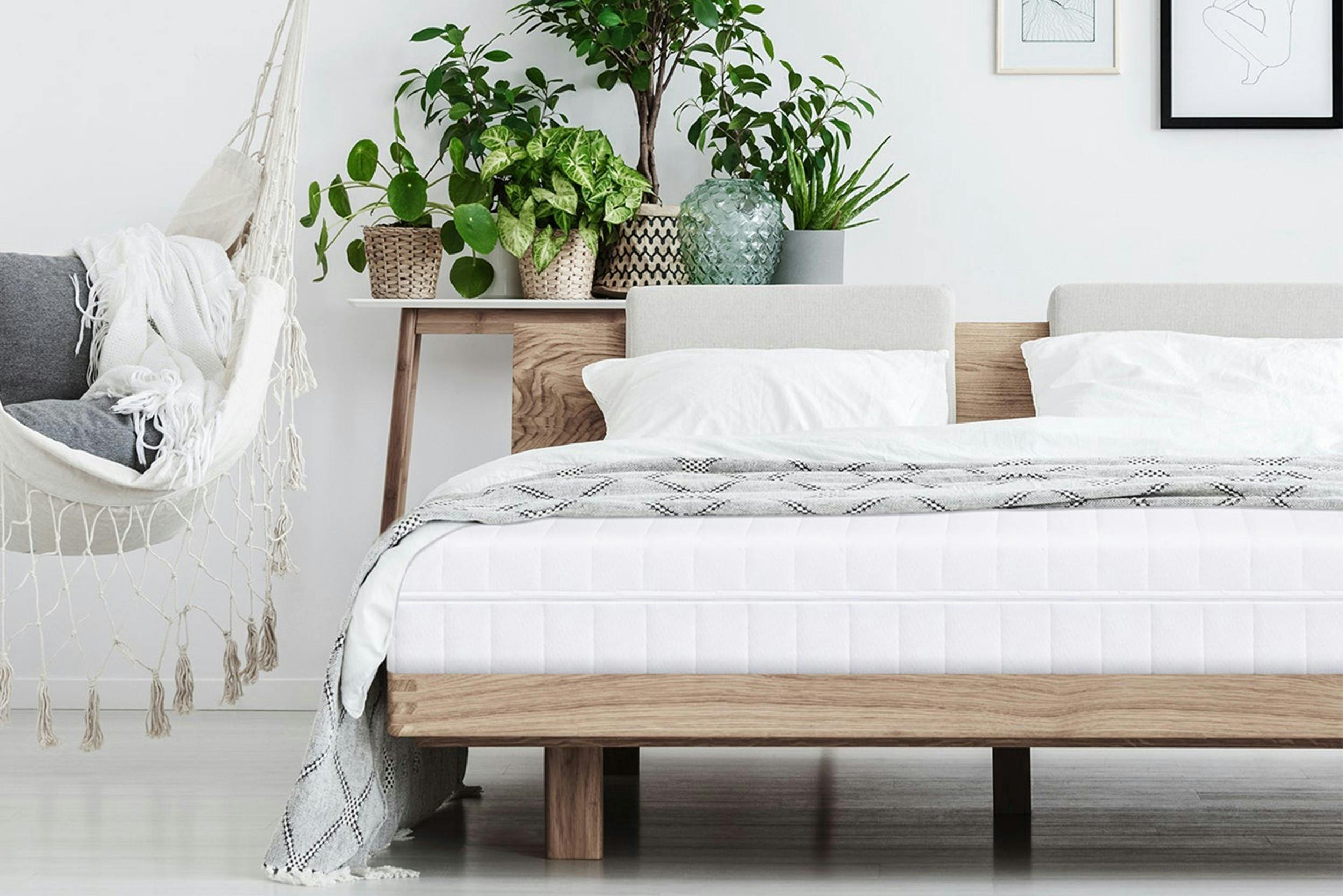 Holzbett ohne Bezug mit weißer Matratze und hellen Kissen