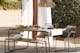 Terrasse in mediterranem Finca-Style mit Gartemöbeln aus Akazienholz und Stahlgestell, die kombiniert sind mit cremefarbenen Outdoor-Textilien, einer Pendellampe in Stroh-Optik und weißen Vorhängen