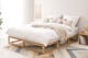 Holzbett mit offenem Bettgestell, weißer Smood-Matratze, beigen Schlafzimmertextilien und einem Würfelregal als Nachttisch