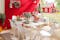 Des meubles de jardin blancs de style scandinave devant un mur de maison rouge typiquement scandinave et décoré d'accessoires rustiques comme un arrosoir en fer blanc et des couronnes de fleurs.