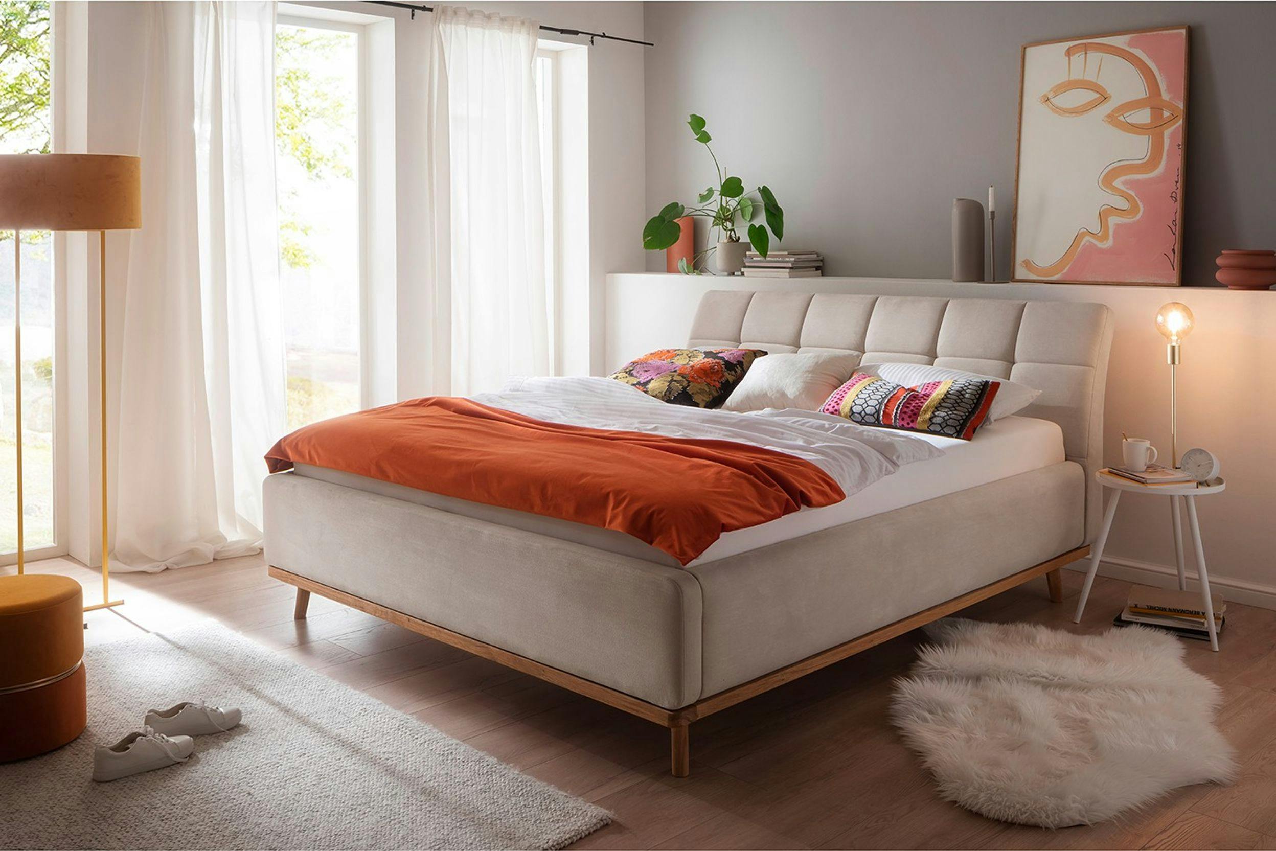 Photo d'un lit avec un cadre de lit capitonné, en tissu beige, dans une chambre cosy