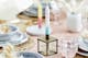 Close-up van materialen en accessoires op een gedekte tafel: echt hout, keramiek, rotan, glas met reliëfornamenten, goudkleurig roestvrij staal en kleurrijke kaarsen in de dip-dye look.