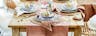 Tavola pasquale e mobili per la sala da pranzo in legno chiaro e rattan, stoviglie di ceramica, bicchieri rosa, posate color oro su runner di cotone, decorato con uova di Pasqua dorate.