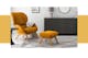 Retro-Sessel aus Samt in Orangegelb mit passendem Hocker auf einem schwarz-weißen Teppich, dazu ein schwarzer Beistelltisch, ein mattgraues Sideboard, ein Deko-Spiegel, eine Tischleuchte aus Beton sowie ein Wandbild mit Audrey Hepburn